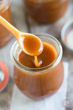 a spoon full of caramel sauce sitting on top of a glass jar filled with liquid