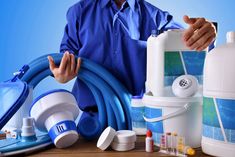 a man holding a blue hose next to several different types of household cleaning supplies on a table