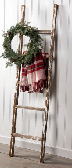 an old ladder with a wreath on it and a plaid blanket hanging from the top