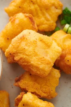 some fried food on a white plate with green onions and dipping sauce in the bowl