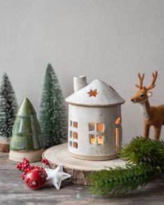 a small white house sitting on top of a wooden table next to christmas trees and ornaments