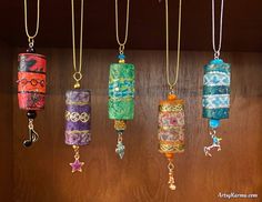 five different colored items hanging from chains on a wooden wall with beads and charms attached to them