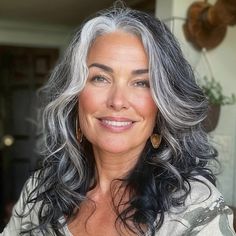 an older woman with gray hair smiling at the camera and wearing gold hoop earrings on her left ear