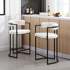 two white bar stools sitting next to each other in front of a kitchen counter