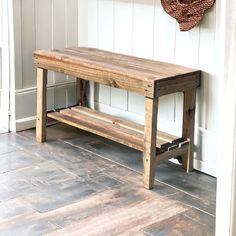 a wooden bench sitting in front of a white wall next to a basket on the floor