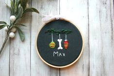 a cross stitch christmas ornament hanging from a hoop on a wooden table next to a potted plant