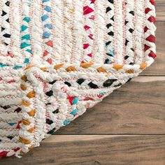 a multicolored rug is laying on the floor next to a wooden floor with a white and red blanket