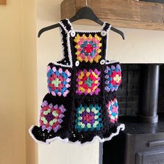 a crocheted dress hanging from a hook in front of a fire place with a fireplace