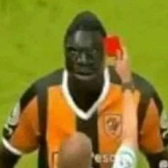 a man in an orange and black uniform holding a red object while standing on a soccer field