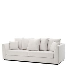 a white couch with many pillows on it's back and side ends, in front of a white wall