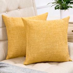 two yellow pillows sitting on top of a white couch next to a potted plant