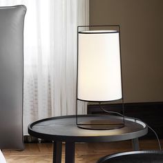 a table with a lamp on it next to a pillow and chair in front of a window