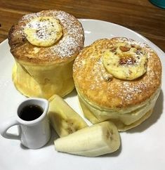 two pancakes with bananas and powdered sugar are on a plate next to a cup of coffee