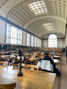 two people sitting at tables in a large room with lots of books on the shelves