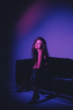 a woman sitting on top of a black couch in front of a purple wall and floor