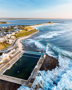 an aerial view of the ocean and beach with large swimming pools in front of it