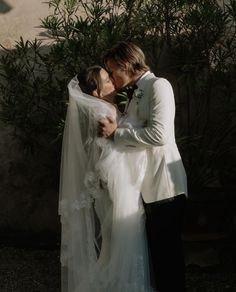 a bride and groom kissing in front of a bush with greenery on the side