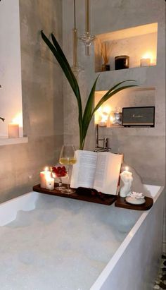 a bathtub with candles and an open book on it's tray next to a potted plant