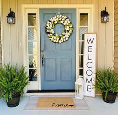 a blue front door with a welcome mat and potted plants