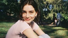 a woman sitting in the grass with her arms crossed and smiling at the camera,