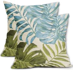 two pillows with blue and green tropical leaves on them, one has a white background