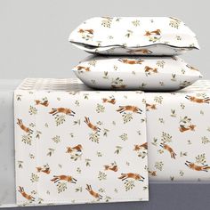 three pillows stacked on top of each other next to two sheets with foxes printed on them