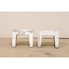 two white stools sitting next to each other on top of a cement floor in front of a wall