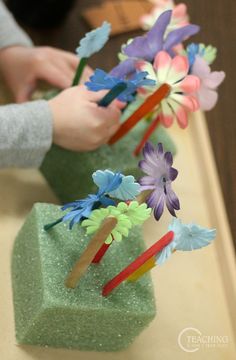 two children are playing with colorful paper flowers in vases on a counter top, while another child is reaching for the flower