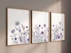 three framed art pieces with flowers on them in a living room wall setting, one is white and the other is purple