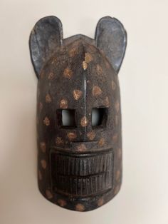 a wooden mask with holes in the middle and ears on it's face, sitting against a white wall