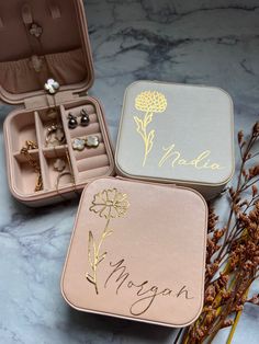 two personalized jewelry boxes sitting on top of a marble counter next to dried flowers