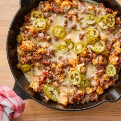 a skillet filled with cheese and vegetables on top of a wooden table next to a napkin