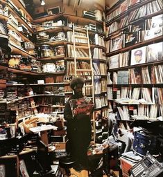 a man standing in front of a bookshelf filled with lots of records and cds