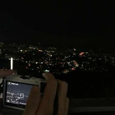 a person taking a photo with their cell phone at night in front of the city lights