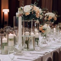 the table is set with candles and vases filled with flowers, greenery, and glassware