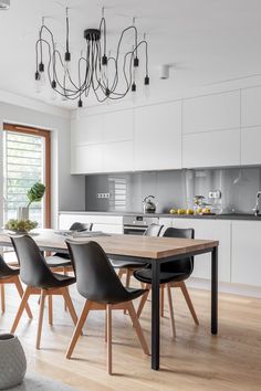 a dining room table with black chairs and a white kitchen in the backround