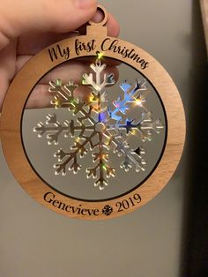 a wooden ornament with a snowflake in the center that reads, my first christmas genieve 2019