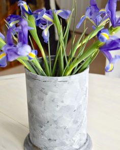 some purple flowers are in a gray vase on a table with white and yellow accents