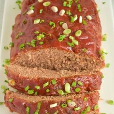 sliced meatloaf on a white plate topped with green onions and pistachio