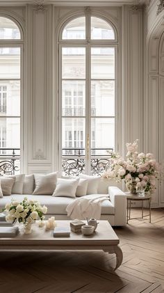 a living room filled with lots of white furniture and flowers on top of a coffee table