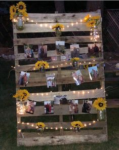 an old pallet is decorated with sunflowers and string lights to display family photos