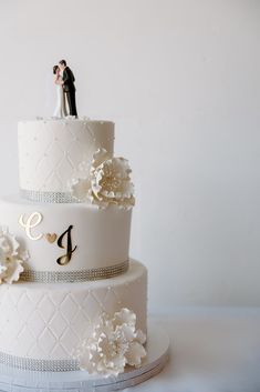 two tiered wedding cake decorated with white flowers and monogrammings on top