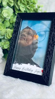 a black frame holds a photo of a dog with glasses and a flower in its mouth