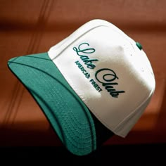 SHIPPING MID MARCH -  It's the summer's favorite club - the Lake Club! Take our design and sport it out on the water for that extra layer of SPF. We love this cursive script and the color matching thread to the bill. The antique white is super crisp! This is the first of this kind of hat, so we can't wait to see how you style it. Tag us on Instagram! @AgencyofSaints Hat Band - 22 ⅘ (adjustable) Crown Height - 4 ¾ Summer Baseball Cap With Letter Print And Flat Bill, Green Baseball Cap For Summer Sports Events, Sporty Summer Six-panel Snapback Hat, Green Snapback Hat For Sports In Summer, Green Snapback Hat For Summer Sports, Green Summer Sports Snapback Hat, Summer Sports Trucker Hat With Embroidered Logo, Retro Sports Hats For Summer, Summer Sports Events Baseball Cap With Flat Brim