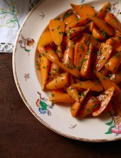 a plate full of cooked carrots on a wooden table with a cloth and napkin