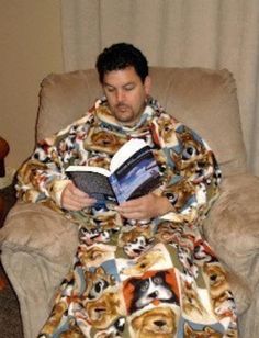 a man sitting in a chair with a blanket on his lap reading a book while wearing a dog print robe