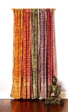 a buddha statue sitting in front of an open window with multicolored curtains behind it