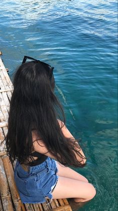 a woman sitting on top of a wooden dock next to the ocean