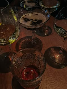 several wine glasses sitting on top of a wooden table next to each other with different wines in them