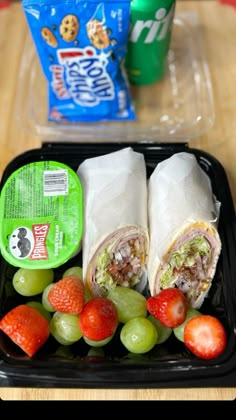 a lunch box with fruit, sandwich wrap and yogurt on the table next to it